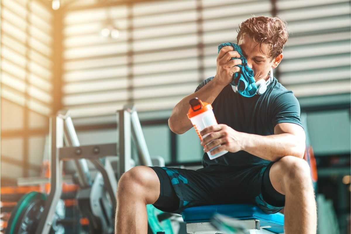 Mann trinkt einen Drink während des Trainings im Fitnessstudio