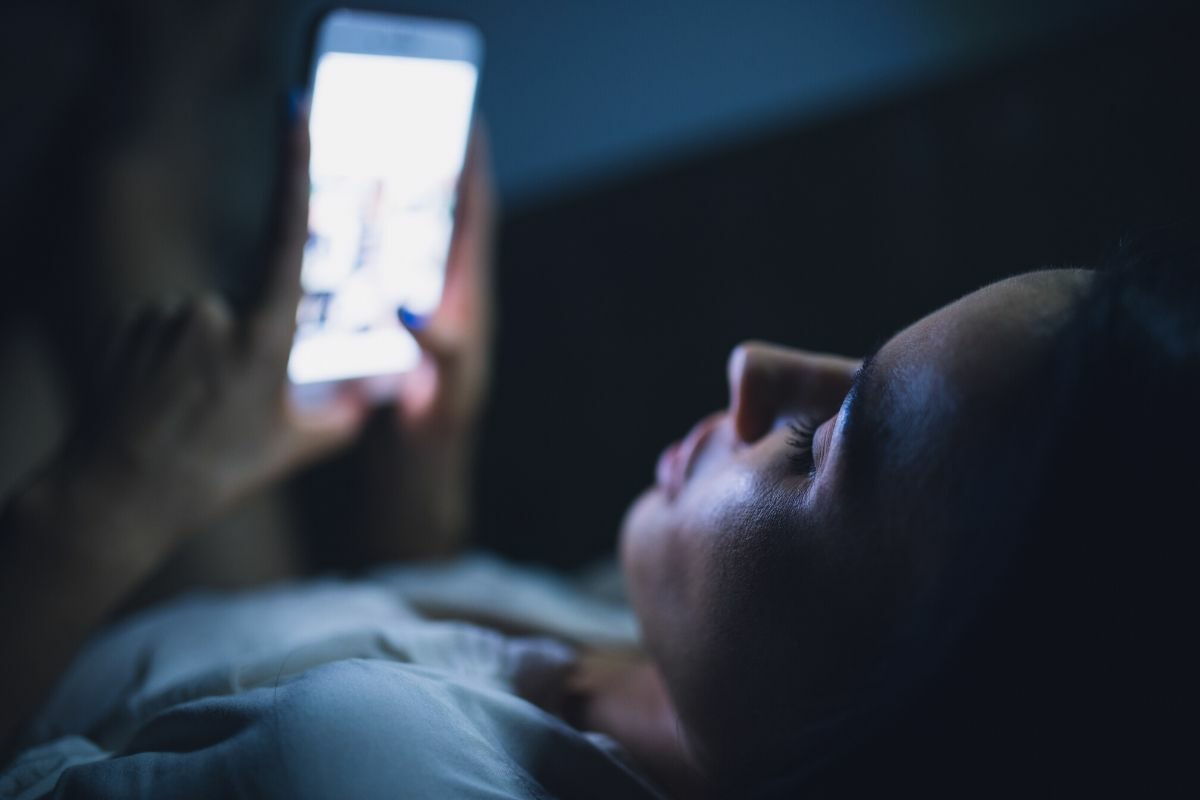 girl looking at cell phone in bed at night